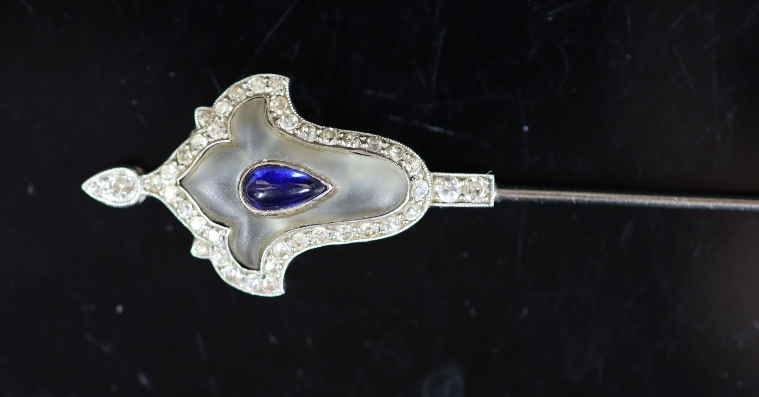 A cased early 20th century platinum, pear shaped cabochon sapphire, diamond chip and frosted rock crystal set jabot pin, in Cartier fitted gilt tooled pink leather box